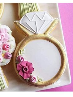 two decorated cookies on a plate next to each other with flowers and an engagement ring