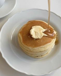 a stack of pancakes on a plate with butter and syrup being drizzled onto them