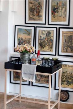 there is a table with flowers and wine glasses on it in front of several framed pictures