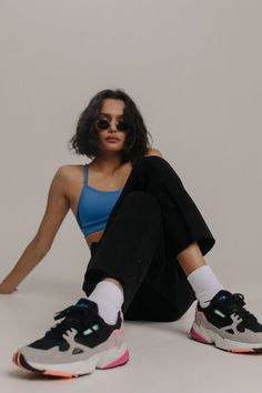 a woman sitting on the ground with her legs crossed wearing black pants and blue sports bra top