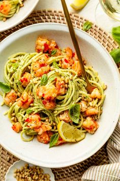 a white bowl filled with pasta and shrimp on top of a woven table cloth next to two plates of food