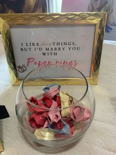 a glass bowl filled with origami pieces next to a sign that says i like things, but i'd marry you