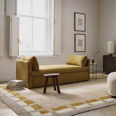 a living room filled with furniture and a large white window above the couch is a coffee table that sits on top of a rug