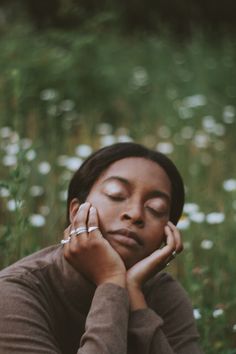 a woman is sitting in the grass with her eyes closed and hands on her face