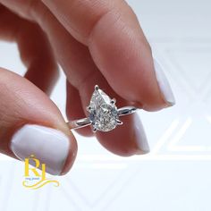 a woman's hand holding a ring with a pear shaped diamond on top of it