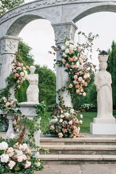 an outdoor garden with statues and flowers on the steps leading up to it, surrounded by greenery