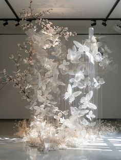 a sculpture made out of plastic flowers and branches in a room with sunlight coming through the window