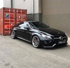 a black car is parked in front of a building with shipping containers on the side