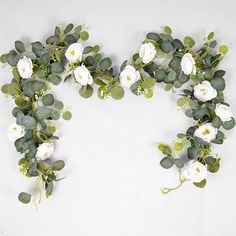 white flowers and green leaves arranged in the shape of a heart on a white background