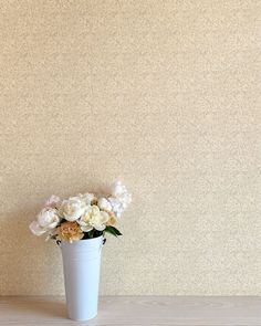 a white vase filled with lots of flowers on top of a wooden table next to a wall