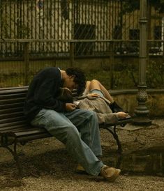 a man and woman sitting on a bench in front of a fence, one kissing the other