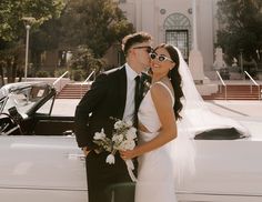 a bride and groom standing in front of a white car