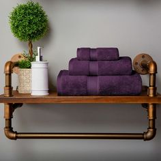 purple towels are stacked on a shelf next to a potted plant and toilet paper