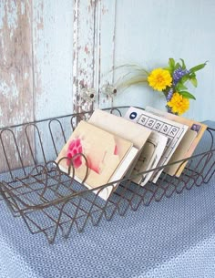 a wire basket with magazines and flowers in it sitting on a blue table cloth next to an old door