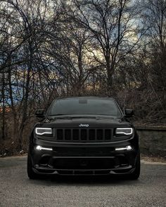 the front end of a black jeep parked on top of a parking lot next to trees