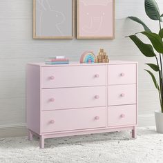 a pink dresser with two pictures on the wall and a potted plant next to it