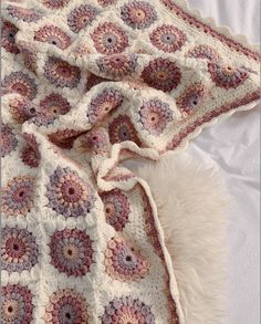 a crocheted blanket is laying on top of a white bed with fluffy pillows