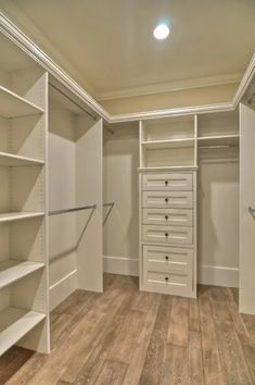 an empty walk in closet with shelves and drawers on the wall, next to a wooden floor