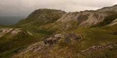 an image of the top of a mountain with clouds in the sky and grass on the ground