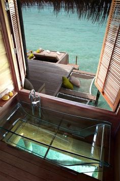 a glass sink in front of a window with the view of water and wooden shutters