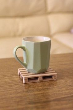 a green coffee cup sitting on top of a wooden pallet next to a white couch