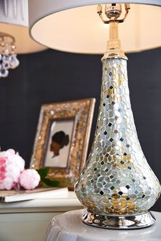 a silver vase sitting on top of a table next to a mirror and lamp shade