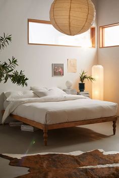 a bed with white sheets and pillows next to a plant in a room filled with windows