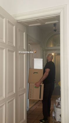 a man holding a cardboard box while standing in an open doorway with the words moving day written on it