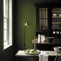 a dining room with green walls and wooden furniture in the corner, along with dishes on a table