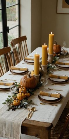 a table set for thanksgiving dinner with candles and pumpkins