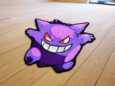 a purple rug with an angry face on the floor next to a wooden floor in a room