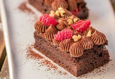 two pieces of chocolate cake with raspberries and nuts on top sitting on a white plate