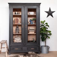 an antique china cabinet with glass doors and shelves in the corner, next to a potted plant