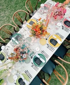 a long table is set with plates, flowers and candles for an outdoor dinner party