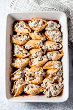 a white casserole dish filled with shells covered in meat and cheese, sitting on a table