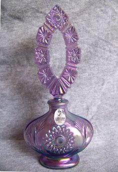 a purple glass vase sitting on top of a gray tablecloth covered floor next to a white wall