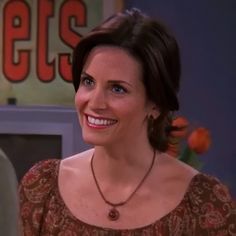 a woman in a brown dress smiling at someone on the television screen with an orange sign behind her