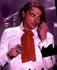 a man in a white shirt and red tie talking on a cell phone while holding a microphone