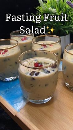 four glasses filled with pudding sitting on top of a wooden table next to a potted plant