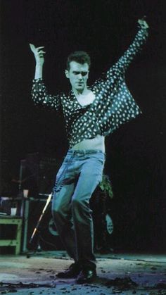 a man is dancing on stage with his arms in the air while wearing jeans and a polka dot shirt