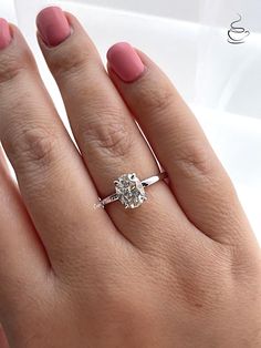 a woman's hand with a diamond ring on top of her finger and pink nail polish