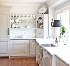 a large kitchen with white cabinets and wooden floors is pictured in this image, there are dishes on the shelves above the sink