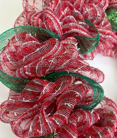 three red and green mesh wreaths sitting on top of a white table next to each other