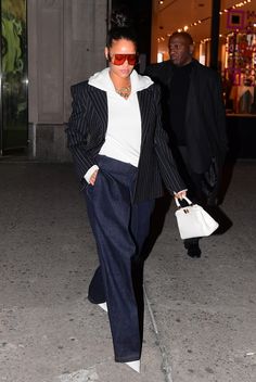 a woman walking down the street carrying a white handbag in her right hand and wearing red sunglasses