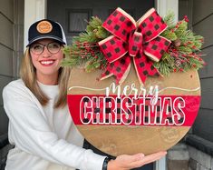 a woman holding up a christmas sign with the words merry christmas on it and a bow