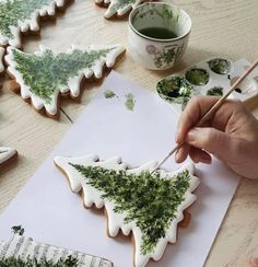 someone is decorating some cookies with green leaves on them and holding a paintbrush