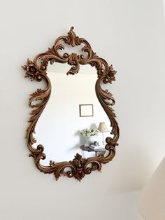 a mirror that is on the wall near a lamp and table with a vase in it