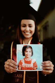 a woman in graduation gown holding up a photo with the graduate's name on it