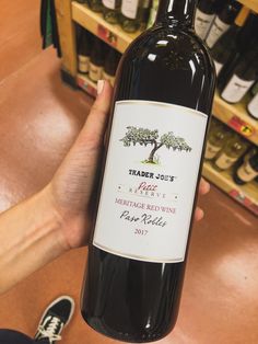 a person holding up a bottle of wine in front of shelves with bottles on it