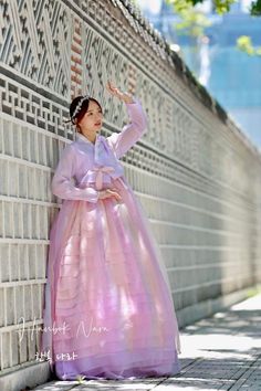 a woman in a long pink dress leaning against a wall with her hand on the side